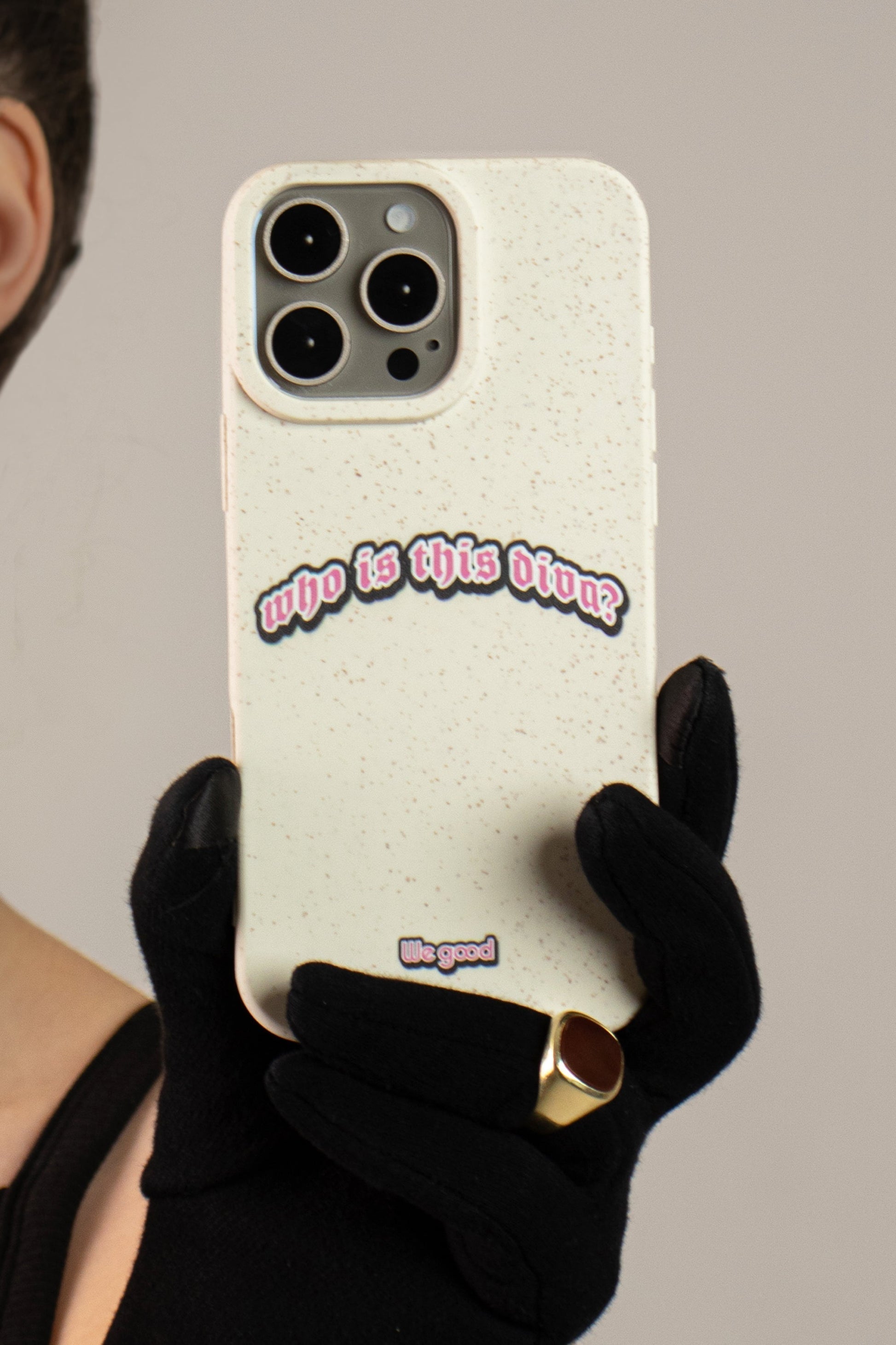 Woman with black gloves in a dress holding a We Good Tpu iPhone case with wheat mix speckled in an off-white color with a pink, white and black 'who is this diva?' gothic text print.