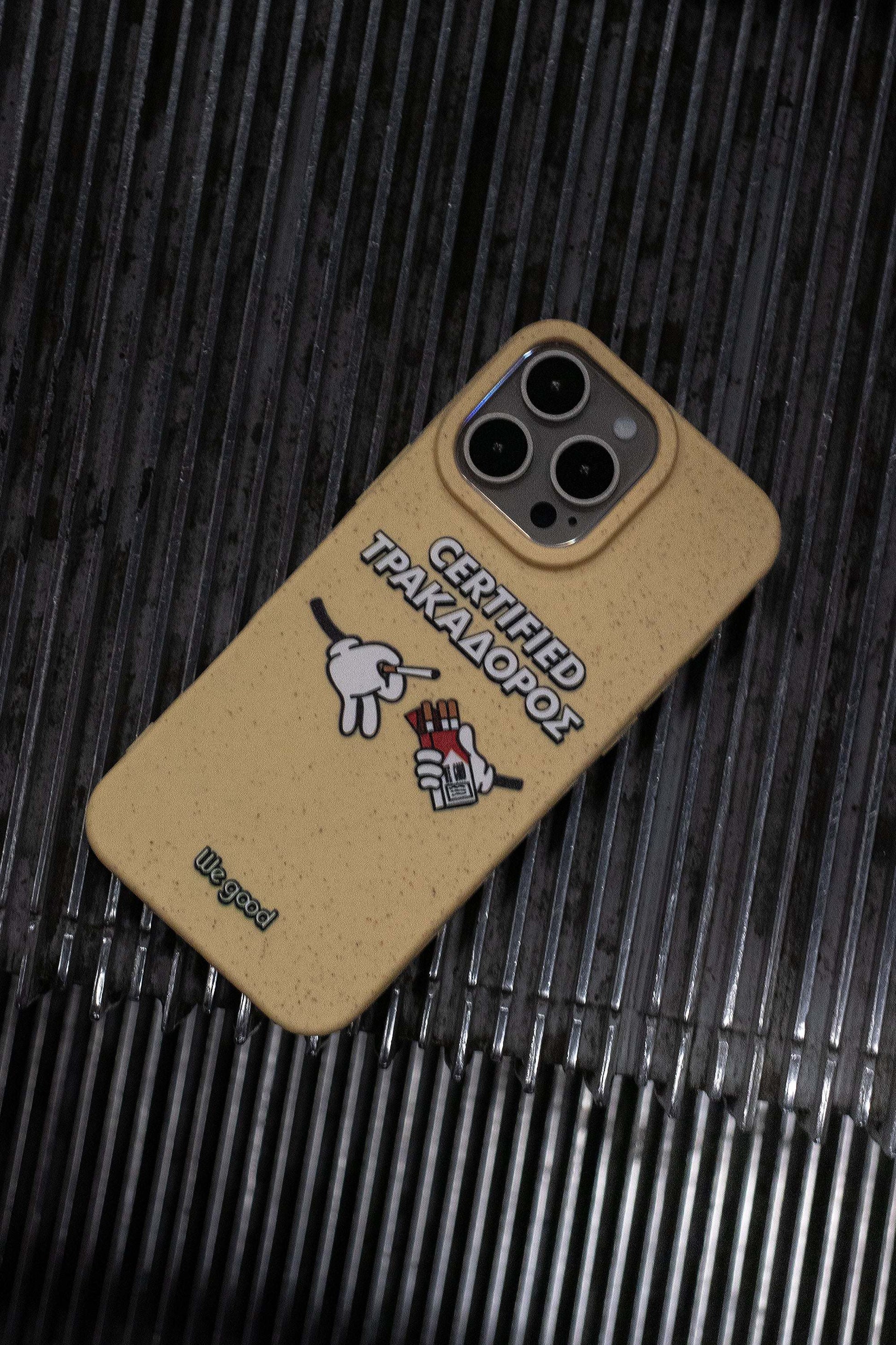 We Good Tpu iPhone case with wheat mix speckled in a canary yellow color with 'certified trakadoros' white and black bold text print and below it two cartoon hands with white gloves with one holding a red pack of cigarettes and the other hand taking one from the pack resting on the steps of an escalator.